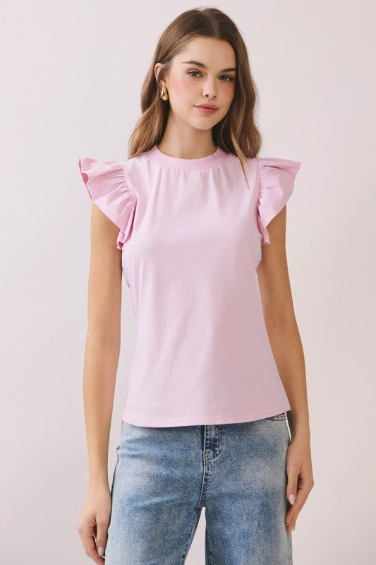 Woman wearing a pink top with ruffled sleeves and blue jeans on a light pink background