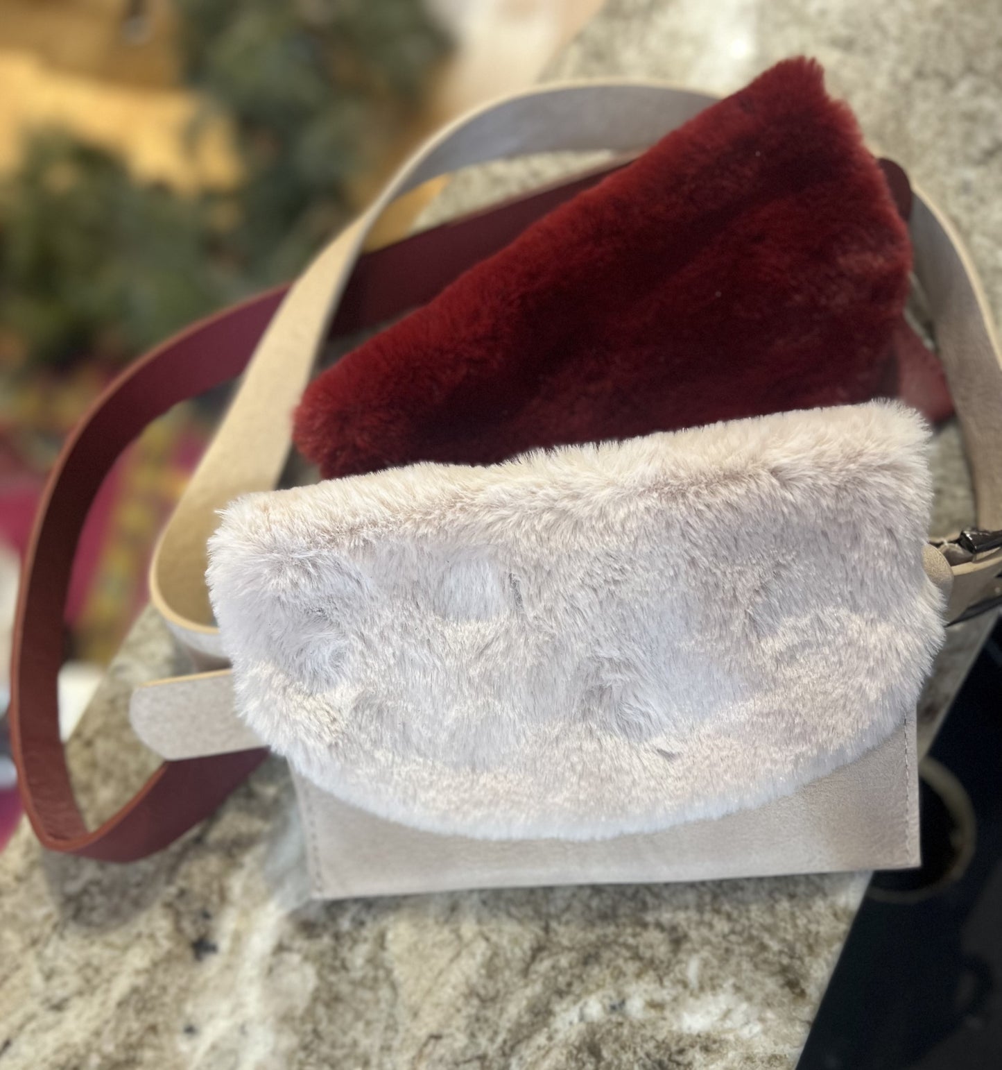 A beige faux fur belt bag attached to a brown leather belt, with the faux fur showing a pink inner lining and a front flap closure.