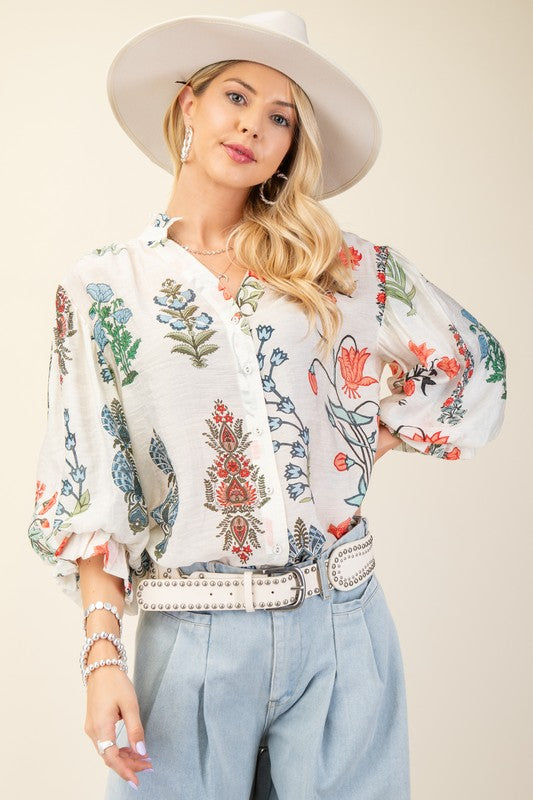 Woman wearing a floral embroidered blouse and white hat against a plain background