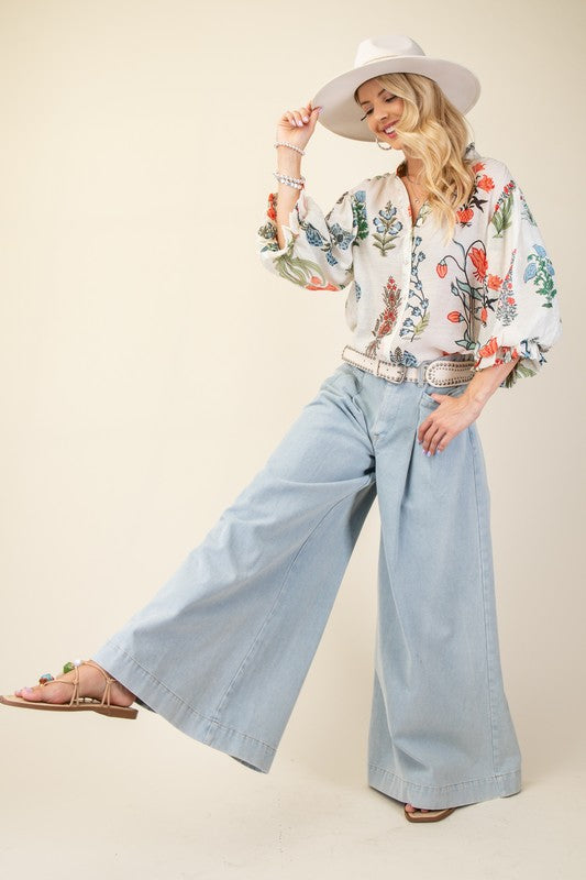 Woman wearing a floral blouse, wide-leg jeans, and a hat on a plain background