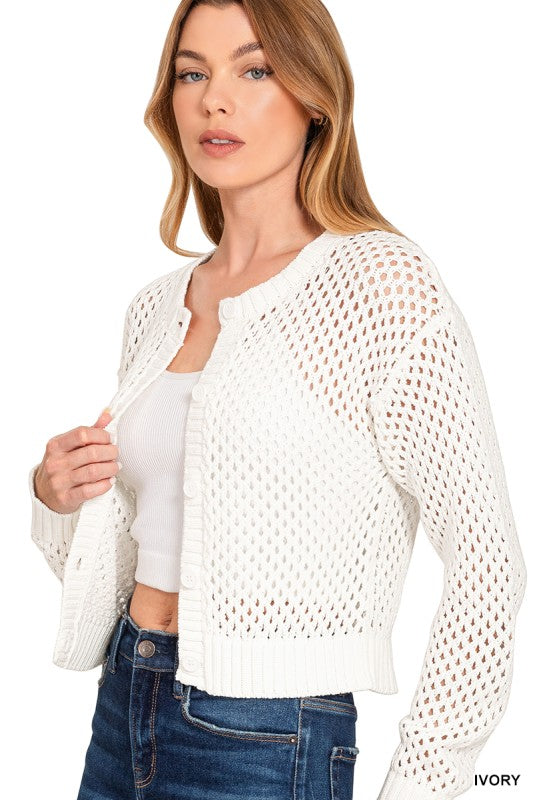 Woman wearing a white open-knit cardigan over a white top with blue jeans on a white background.