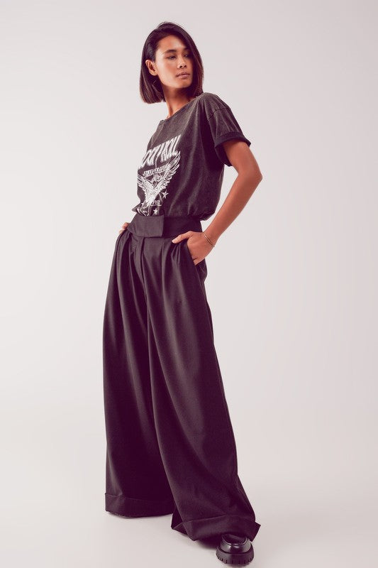 A model wearing black wide leg trousers with a high waist and cuff at the hem, paired with a graphic t-shirt.