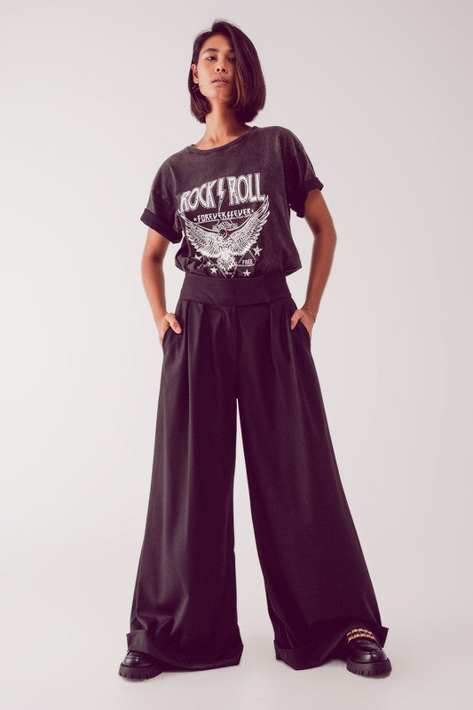 A model wearing black wide leg trousers with a high waist and cuff at the hem, paired with a graphic t-shirt.