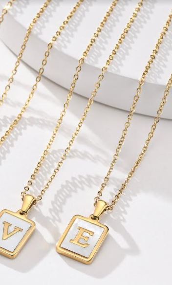 Two gold chain necklaces with square mother of pearl pendants, displaying different initials.