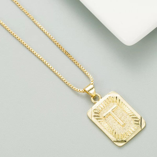 A gold initial necklace with a pendant on a person wearing a light blue sweater.